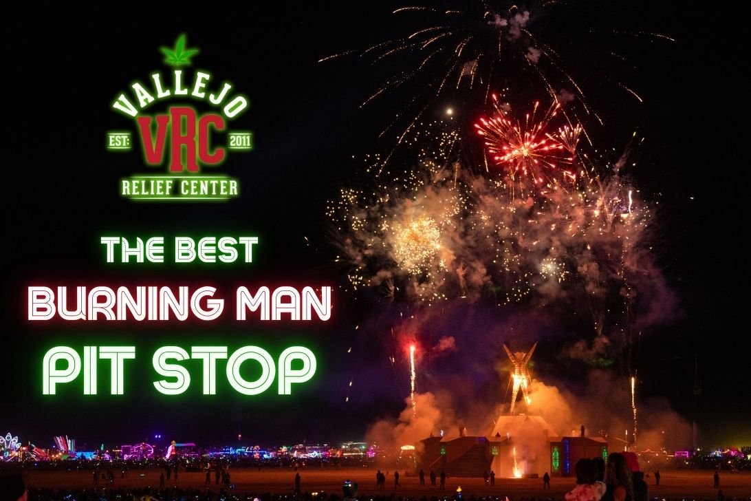 Nighttime fireworks explode over the Burning Man festival, with the wooden Man structure glowing in flames. Neon text on the left reads “Vallejo Relief Center – Your Best Burning Man Pit Stop,” styled in green and red festival lights.
