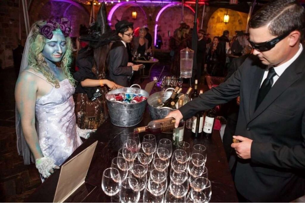 People dressed in Halloween costumes at a lively Pagan Ball event, with a zombie bride and guests enjoying drinks at the bar.