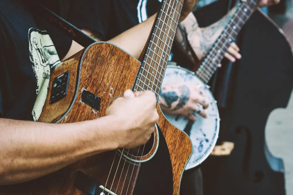 Close-up of musicians playing acoustic instruments, including a guitar and banjo, with hands and strings in sharp focus.