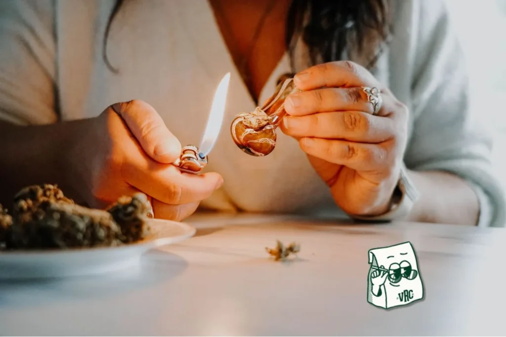 Person lighting a cannabis pre-roll with flower on a plate nearby and VRC mascot bag logo.
