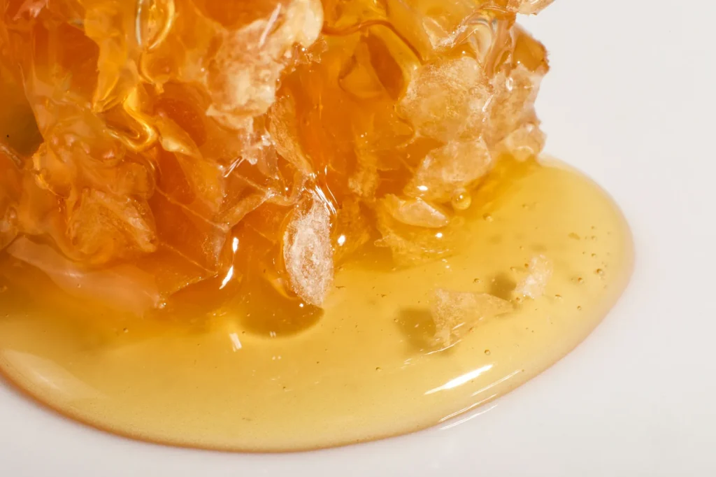 Glossy, layered cannabis concentrate melting into a liquid sauce pool with visible shatter fragments